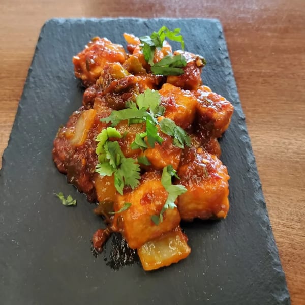 Indian chili paneer, a vibrant orange dish with green cilantro, served on a dark slate.