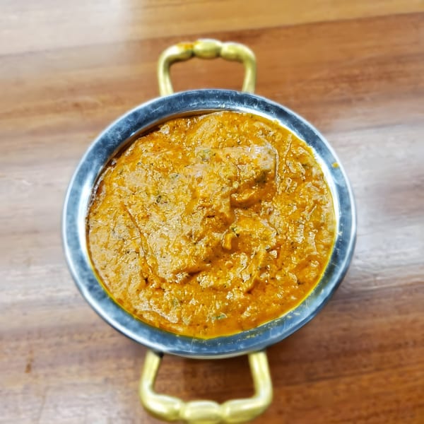 Overhead view of a metal handi bowl filled with rich, orange Indian curry on a wooden table.