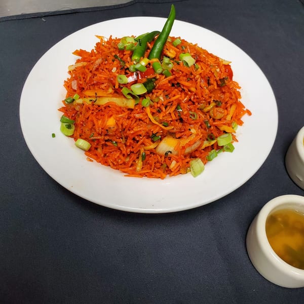 Indian fried rice, vibrant orange with green chilies and scallions, served on a white plate.