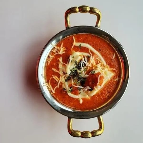 Overhead view of Indian butter chicken in a metal handi, garnished with cream and herbs.