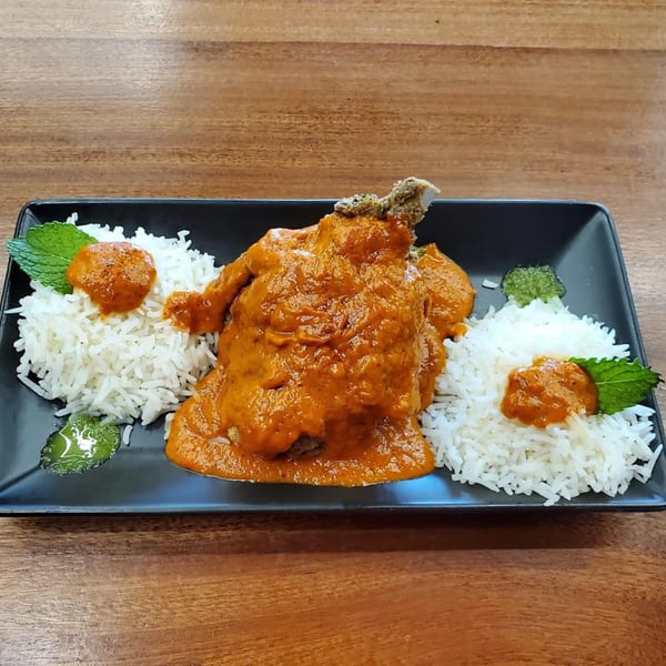Indian chicken curry with rice, garnished with mint leaves and sauce, on a black plate.